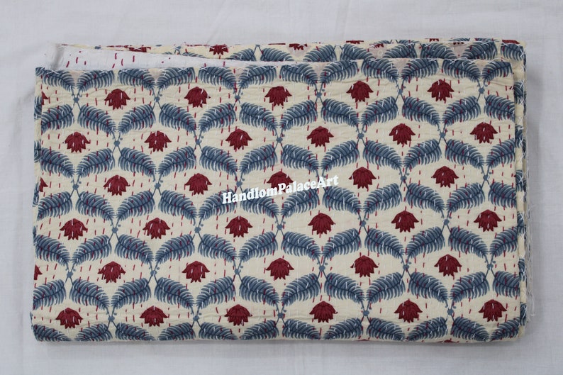 Puede incluir: Una tela doblada con fondo blanco y un patr&oacute;n repetitivo de hojas azules y flores rojas. La tela tiene una textura de tejido a mano y es ideal para acolchar o proyectos de artesan&iacute;a.