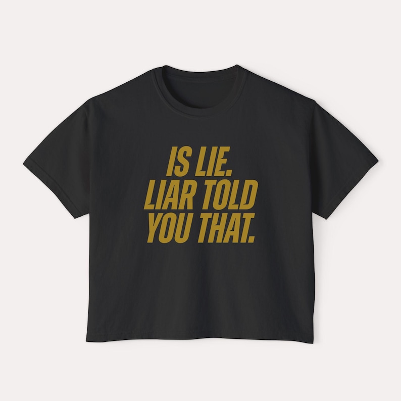 K&ouml;nnte beinhalten: Schwarzes T-Shirt mit dem goldenen Text "IS LIE. LIAR TOLD YOU THAT.". Das T-Shirt mit Rundhalsausschnitt ist ein schlichtes Design, ideal f&uuml;r den Alltag. Der Text ist mittig auf der Vorderseite platziert.