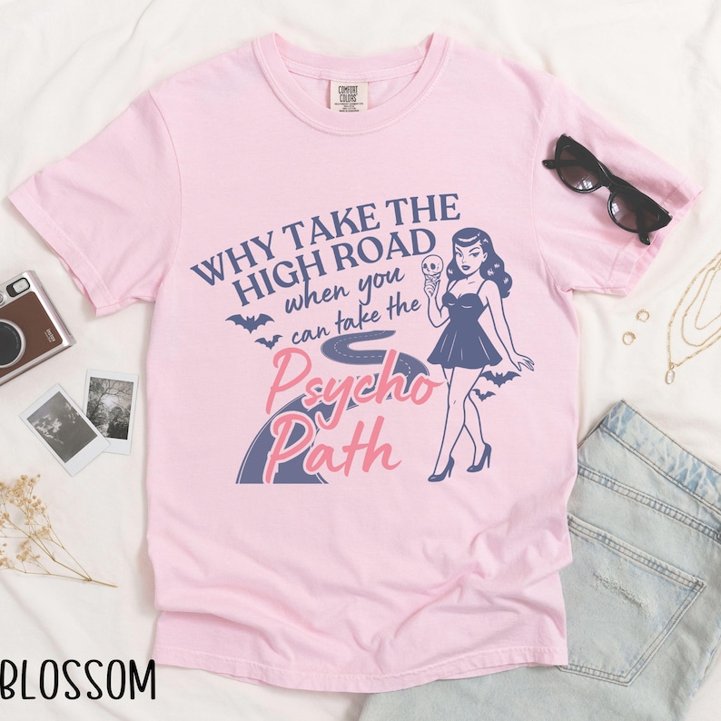 May include: A light pink t-shirt with the text "Why take the high road when you can take the Psycho Path" and a graphic of a woman holding a skull. The word "Blossom" is at the bottom left.