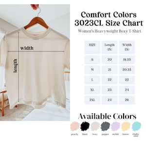 Peut inclure: Un t-shirt beige Comfort Colors 3023CL, de coupe carr&eacute;e et de poids fort, suspendu &agrave; un cintre en bois. L'image comprend un tableau des tailles avec des mesures en pouces et une palette de couleurs avec p&ecirc;che, noir, ivoire, poivre, orchid&eacute;e, beurre et menthe craie.