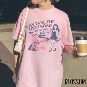 May include: A light pink t-shirt with the text "WHY TAKE THE HIGH ROAD when you can take the Psycho Path" and a graphic of a woman in a dress. The word "BLOSSOM" is printed in the bottom right corner.