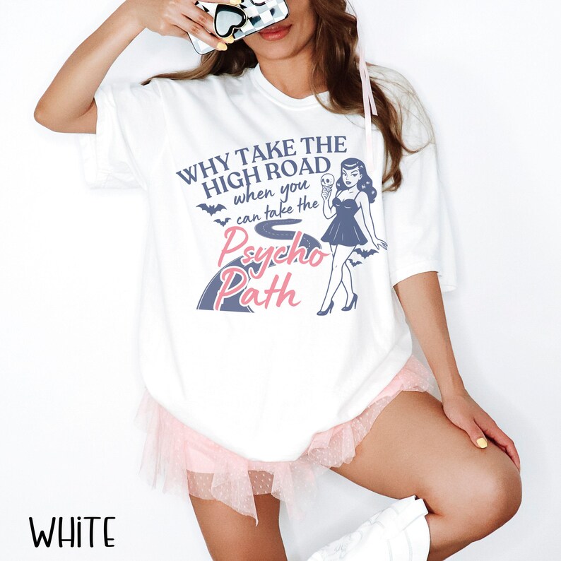 May include: White t-shirt with the text "WHY TAKE THE HIGH ROAD when you can take the Psycho Path" and a graphic of a woman holding an ice cream cone. The shirt also has bat graphics.