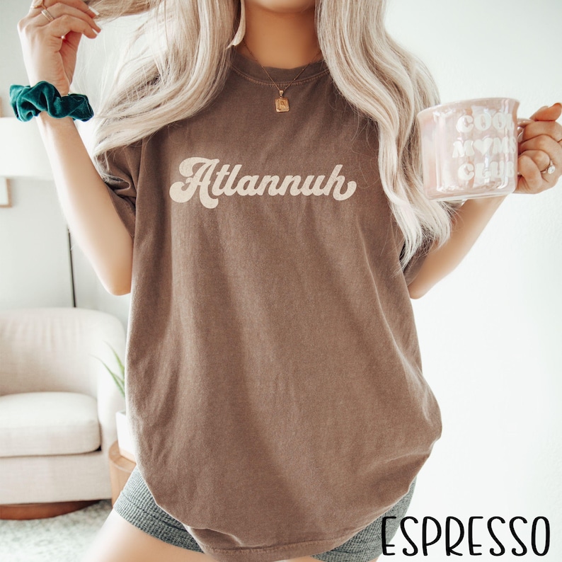 May include: Espresso-colored t-shirt with the word "Atlannuh" in a retro font. The shirt is a solid color and has a relaxed fit. The word "Espresso" is printed at the bottom of the image.
