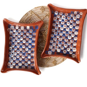 May include: Two terracotta serving dishes with a white and blue geometric pattern. The dishes are on a woven placemat.