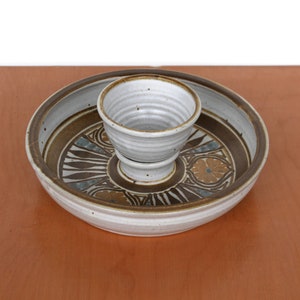 May include: A white ceramic serving dish with a brown and blue geometric design. A smaller white ceramic bowl sits inside the larger dish.