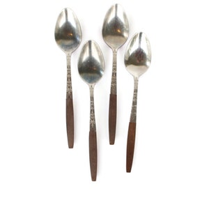 Puede incluir: Cuatro cucharas de plata con mangos de madera marrón. Las cucharas están dispuestas en fila, con los mangos apuntando hacia abajo.