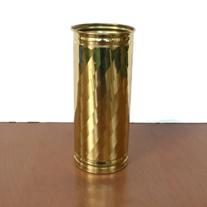 Puede incluir: Un jarrón de metal dorado con un patrón de diamante. El jarrón es cilíndrico y tiene un acabado liso y pulido.