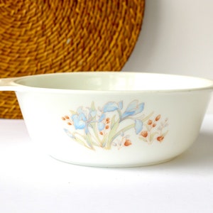 May include: White ceramic bowl with two handles. The bowl features a floral design with blue irises and brown stems on a white background.