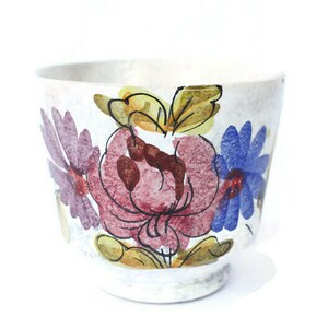 Puede incluir: Una taza de cerámica blanca con un diseño floral. Las flores están pintadas en tonos de rosa, azul, amarillo y marrón.