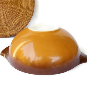May include: A brown and yellow glass mixing bowl with a white interior. The bowl has a rounded shape and two handles.