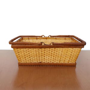 May include: A rectangular woven basket with brown handles. The basket is made of natural materials and has a light brown color.