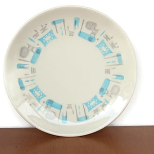 Op de afbeelding: Een wit keramiek bord met een blauw en grijs geometrisch patroon rond de rand. Het patroon bevat gestileerde vormen en lijnen.