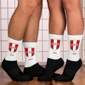 May include: White socks with black heels and toes, featuring the Peruvian Football Federation (FPF) logo. The logo is a red and white shield with the letters "FPF" and the word "PERU" below. The socks are worn by two people.