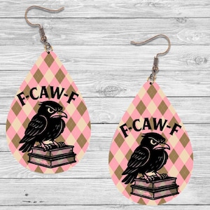 K&ouml;nnte beinhalten: Tropfenf&ouml;rmige Ohrringe mit einem rosa-beigen Rautenmuster. Jeder Ohrring zeigt eine schwarze Kr&auml;he, die auf B&uuml;chern sitzt, mit dem Text "F-CAW-F" dar&uuml;ber. Die Ohrringe haben kupferfarbene Haken.