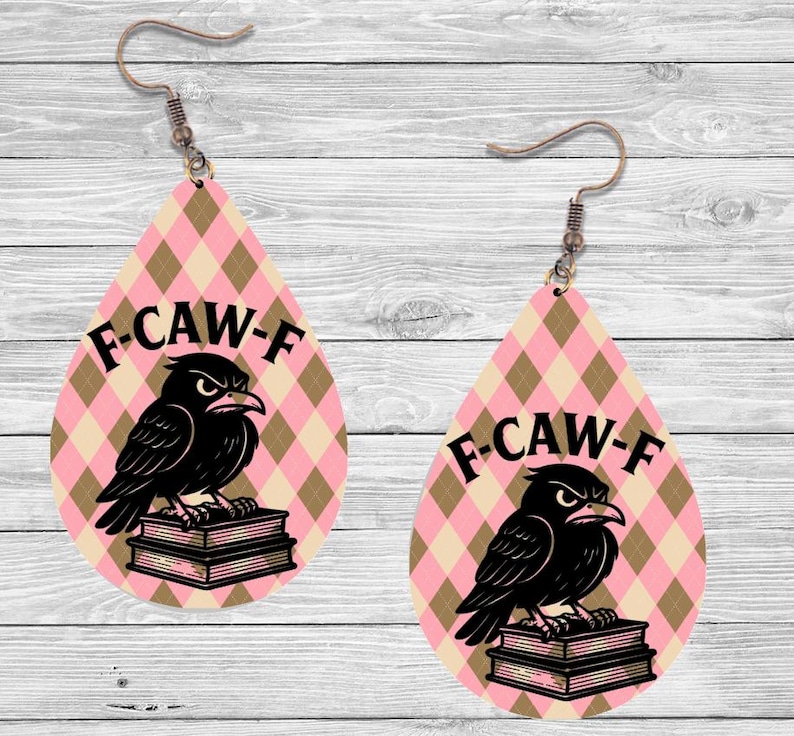 K&ouml;nnte beinhalten: Tropfenf&ouml;rmige Ohrringe mit einem rosa-beigen Rautenmuster. Jeder Ohrring zeigt eine schwarze Kr&auml;he, die auf B&uuml;chern sitzt, mit dem Text "F-CAW-F" dar&uuml;ber. Die Ohrringe haben kupferfarbene Haken.