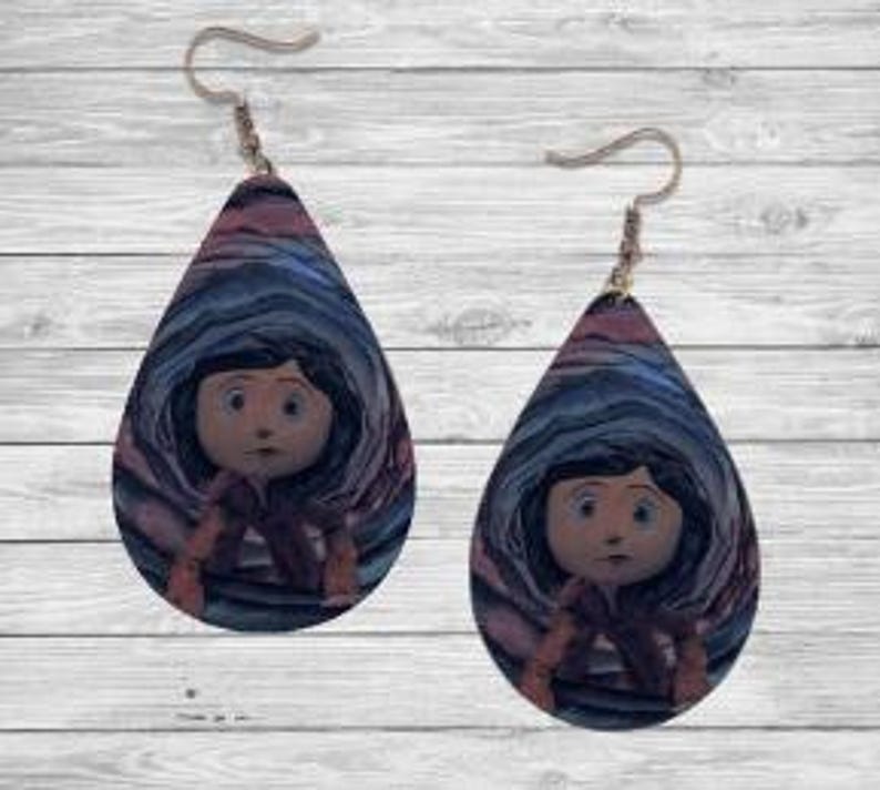 Peut inclure: Paire de boucles d'oreilles en forme de goutte d'eau avec une image de dessin anim&eacute; d'une fille aux cheveux noirs et aux yeux bleus. Les boucles d'oreilles ont un fond tourbillonnant bleu, rose et violet. Les crochets d'oreilles sont dor&eacute;s.
