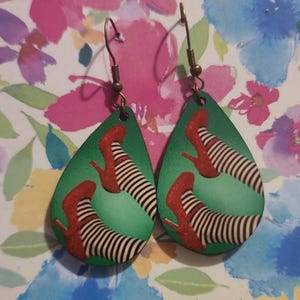 May include: A pair of green teardrop-shaped earrings with a red and white striped design of a pair of ruby slippers.