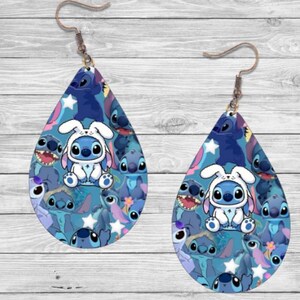 May include: A pair of blue teardrop-shaped earrings featuring a pattern of Stitch characters from the Disney film Lilo & Stitch. The earrings have a silver hook.