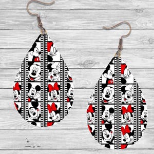 Op de afbeelding: Een paar druppelvormige oorbellen met een zwart-wit filmstripontwerp. De oorbellen tonen afbeeldingen van Mickey en Minnie Mouse met rode accenten en strikken. Ze hebben bronzen oorhaken.