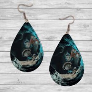 Peut inclure: Une paire de boucles d'oreilles en forme de goutte d'eau avec un motif bleu fonc&eacute; et sarcelle. Les boucles d'oreilles pr&eacute;sentent une illustration fantaisiste de personnages dans un cadre fantastique. Elles sont suspendues &agrave; des crochets d'oreilles argent&eacute;s.