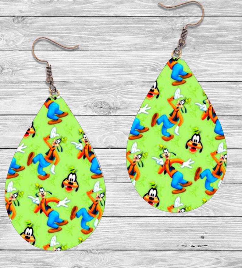 Op de afbeelding: Druppelvormige oorbellen met een groene achtergrond met een patroon van een stripfiguur in oranje, blauw en wit. De oorbellen hebben een koperkleurige haak.