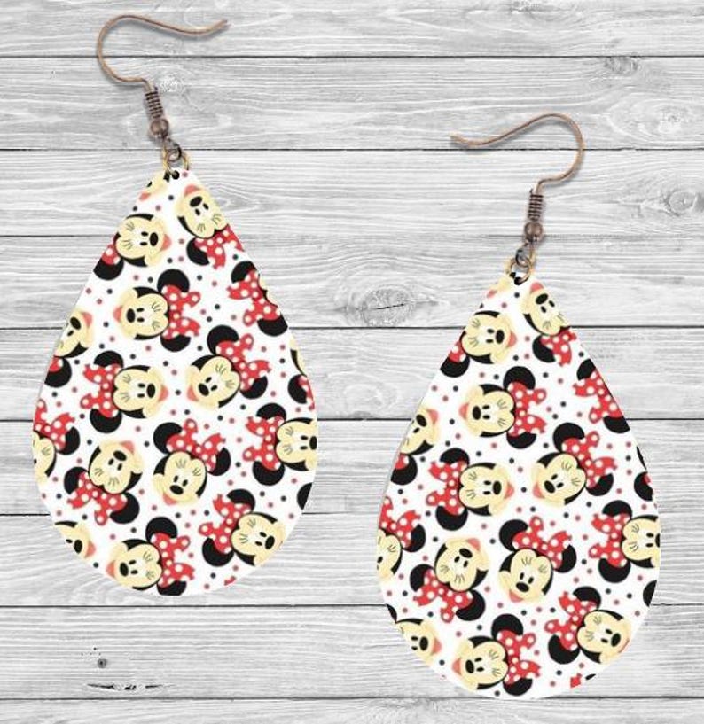 Op de afbeelding: Een paar druppelvormige oorbellen met een herhalend patroon van een stripfiguurgezicht met een rode strik op een witte achtergrond. De oorbellen hebben een bronzen haak.