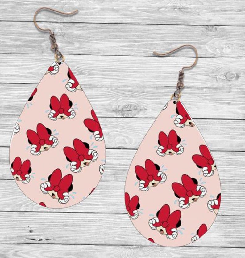 Op de afbeelding: Druppelvormige oorbellen met een lichtroze achtergrond en een herhalend patroon van Minnie Mouse-gezichten met rode strikken. De oorbellen hebben bronzen oorhaken.