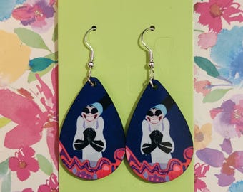May include: A pair of teardrop-shaped dangle earrings featuring a graphic illustration of a character with a wide grin, wearing a white coat and black gloves against a dark blue background, with a red and orange wavy pattern at the bottom edge.