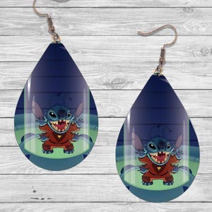 May include: A pair of teardrop-shaped earrings featuring a blue and green image of Stitch from Lilo & Stitch. Stitch is in a glass tube wearing a red and blue spacesuit. The earrings have a silver hook.