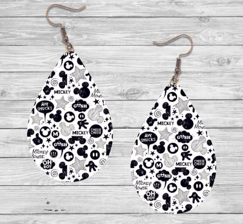 Op de afbeelding: Een paar druppelvormige oorbellen met een zwart-wit Mickey Mouse-ontwerp. De oorbellen hebben verschillende Mickey Mouse-thema's, waaronder sterren, tekstballonnen en de woorden "Mickey Mouse" en "Cheese Cheese". De oorbellen hebben bronzen oorhaken.