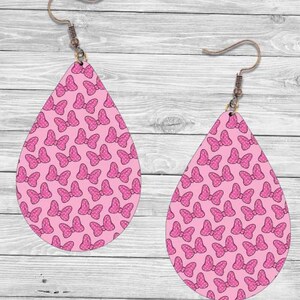 Op de afbeelding: Twee druppelvormige oorbellen met een roze strikpatroon. De strikken zijn donkerder roze met witte stippen. De oorbellen hebben bronzen oorhaken.