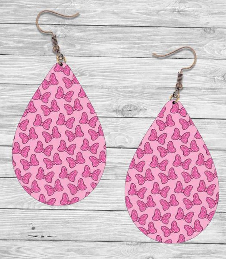 Op de afbeelding: Twee druppelvormige oorbellen met een roze strikpatroon. De strikken zijn donkerder roze met witte stippen. De oorbellen hebben bronzen oorhaken.