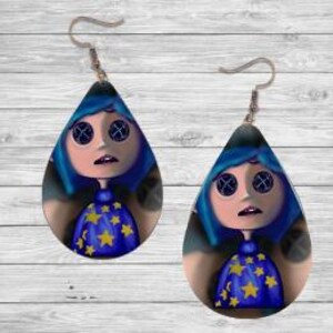 Peut inclure: Boucles d'oreilles en forme de goutte d'eau repr&eacute;sentant un personnage de dessin anim&eacute; aux cheveux bleus, aux yeux en forme de boutons et une robe bleue orn&eacute;e d'&eacute;toiles jaunes. Les boucles d'oreilles ont des fermoirs en forme de crochet de couleur argent&eacute;e.