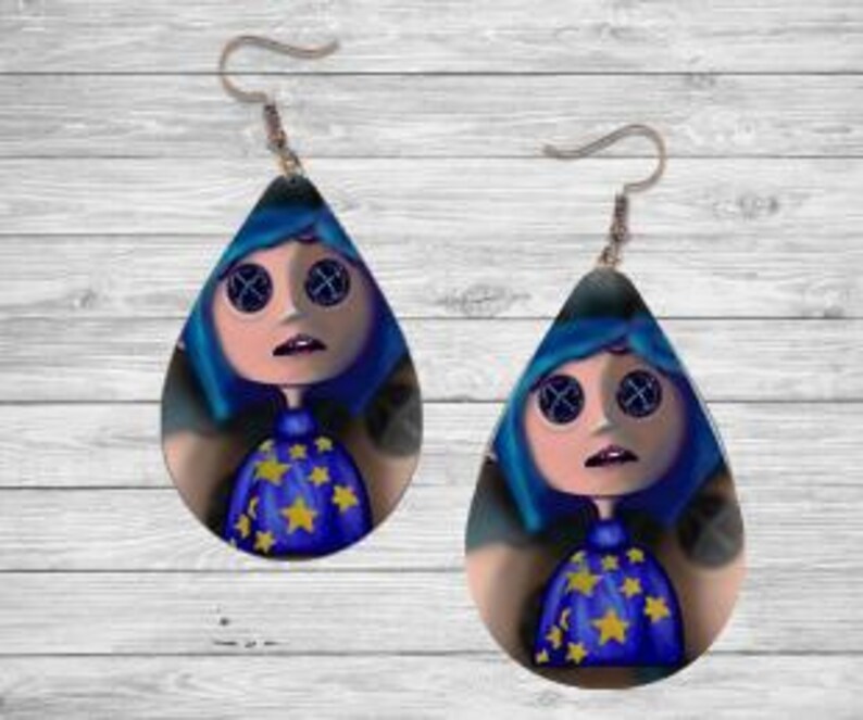 Peut inclure: Boucles d'oreilles en forme de goutte d'eau repr&eacute;sentant un personnage de dessin anim&eacute; aux cheveux bleus, aux yeux en forme de boutons et une robe bleue orn&eacute;e d'&eacute;toiles jaunes. Les boucles d'oreilles ont des fermoirs en forme de crochet de couleur argent&eacute;e.