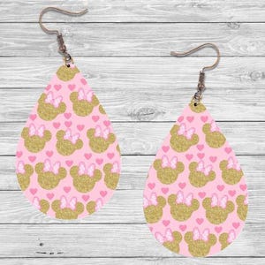 Op de afbeelding: Een paar druppelvormige oorbellen met een roze achtergrond. De oorbellen hebben een patroon van goudglitter muizenkoppen met roze strikjes en kleine roze hartjes. De oorbellen hebben oorhaken in bronskleur.