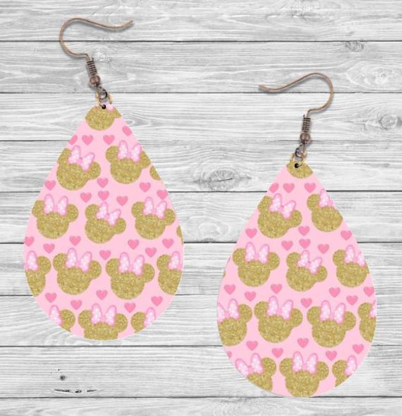 Op de afbeelding: Een paar druppelvormige oorbellen met een roze achtergrond. De oorbellen hebben een patroon van goudglitter muizenkoppen met roze strikjes en kleine roze hartjes. De oorbellen hebben oorhaken in bronskleur.