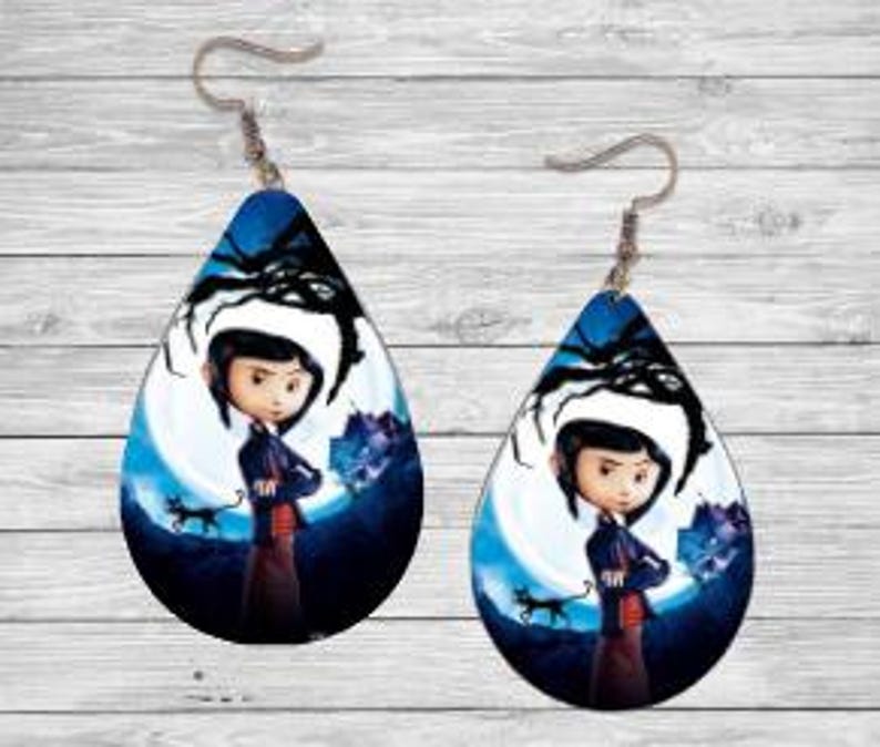 Peut inclure: Paire de boucles d'oreilles en forme de goutte d'eau avec un personnage de dessin anim&eacute; devant une pleine lune, un chat noir et une toile d'araign&eacute;e. Les boucles d'oreilles ont des crochets d'oreille argent&eacute;s et un fond bleu et noir.