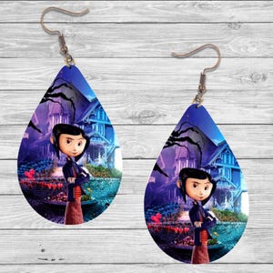 Peut inclure: Boucles d'oreilles en forme de goutte d'eau avec un personnage de dessin anim&eacute; devant une maison. Les boucles d'oreilles ont un fond bleu fonc&eacute; avec un motif de maison et d'arbre. Le personnage porte une veste noire et une jupe marron.