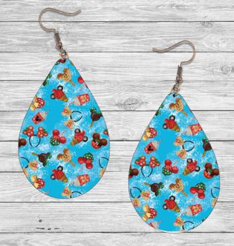 Op de afbeelding: Druppelvormige oorbellen met een lichtblauwe achtergrond en een herhalend patroon van stripfiguren in rood, bruin en geel. De oorbellen hebben zilverkleurige oorhaken.