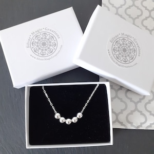 May include: A silver necklace with a row of five round beads in a white box with a black interior. The box has a sticker with the text "Silver Magic Creations" and a website address.