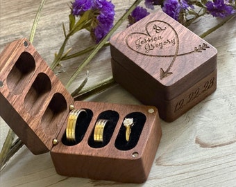 May include: A wooden ring box with three compartments for rings. The box is made of dark wood and has a velvet lining. The box is engraved with the names "Jessica & Gregory" and the date "12.22.23".