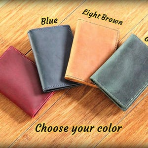May include: Four leather wallets in red, blue, light brown, and green are displayed on a wooden surface. The text "Choose your color" is at the bottom. Each wallet is rectangular with stitched edges.