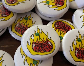 Puede incluir: Una colección de botones redondos blancos con un gráfico de dos cerezas rojas con un diseño de estampado de leopardo en llamas. Las cerezas están sobre una llama amarilla con hojas verdes.