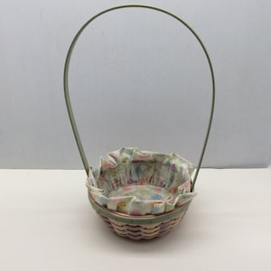 May include: A small, woven basket with a green handle and a white fabric liner with a colorful floral pattern. The basket is perfect for Easter or spring decor.