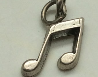 May include: A silver charm in the shape of two musical notes. The charm has a loop at the top for attaching to a bracelet or necklace.