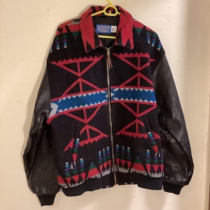 May include: A black and red Pendleton jacket with leather sleeves. The jacket has a geometric pattern and a zipper closure.