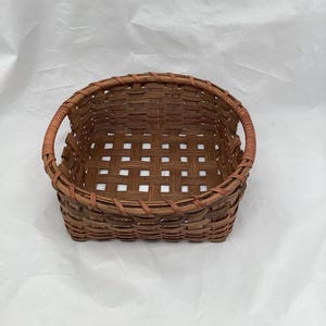 May include: A woven brown basket with two handles. The basket is made of natural materials and has a square shape.