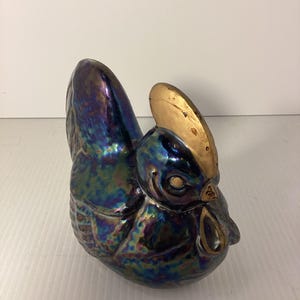 May include: A ceramic rooster figurine with iridescent blue, green, and purple glaze. The rooster's comb is gold.