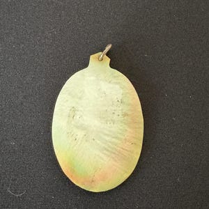 May include: A light green oval pendant with a silver loop at the top. The pendant has a textured surface and a subtle iridescent sheen.