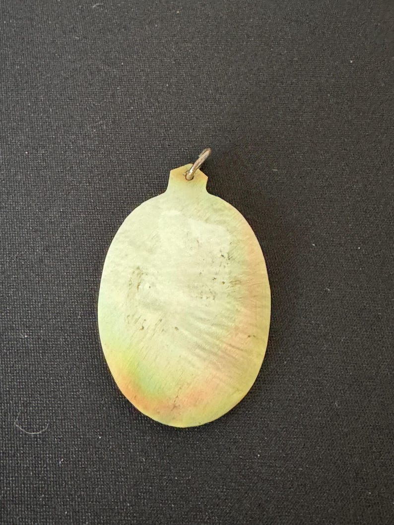 May include: A light green oval pendant with a silver loop at the top. The pendant has a textured surface and a subtle iridescent sheen.